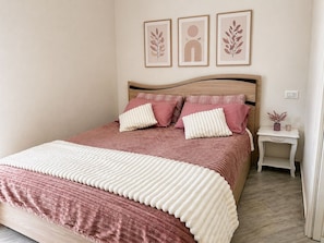 A neatly made bed with a pink and white bedspread, two pillows, and a bedside table with a vase.