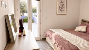 Quarto com cama, mesa de cabeceira e porta para área externa.