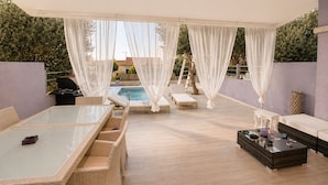 Uma área externa coberta com piscina, espreguiçadeiras, uma mesa e um sofá de vime.