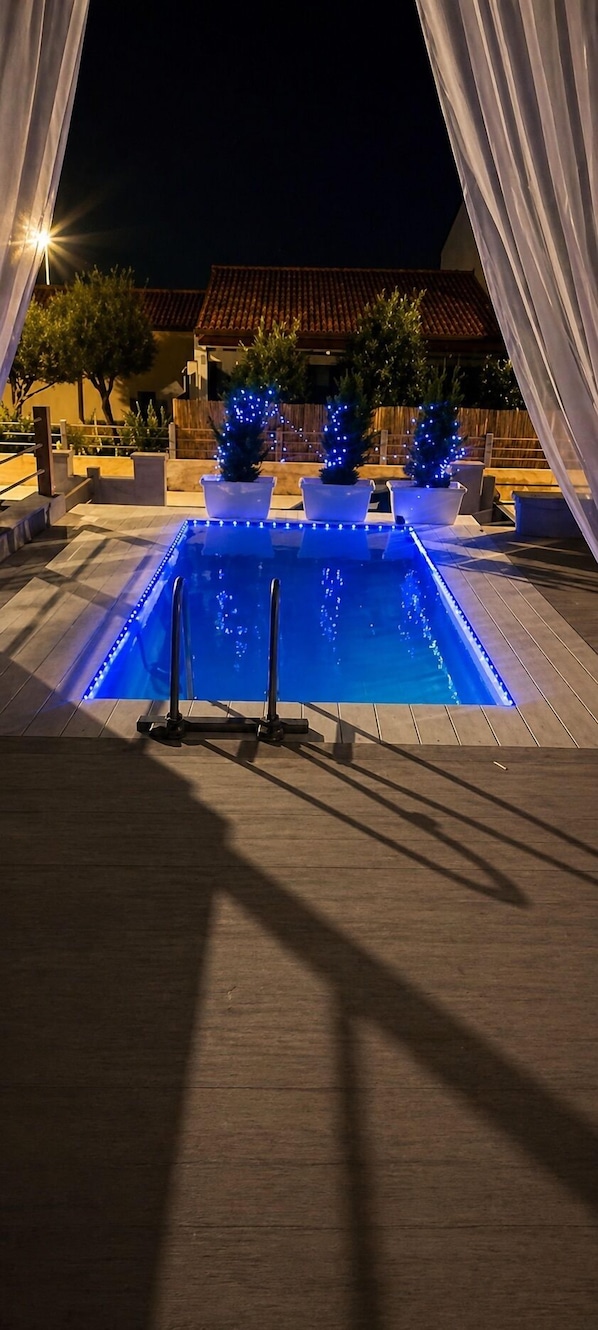 A swimming pool with blue LED lights, surrounded by potted plants and outdoor furniture.