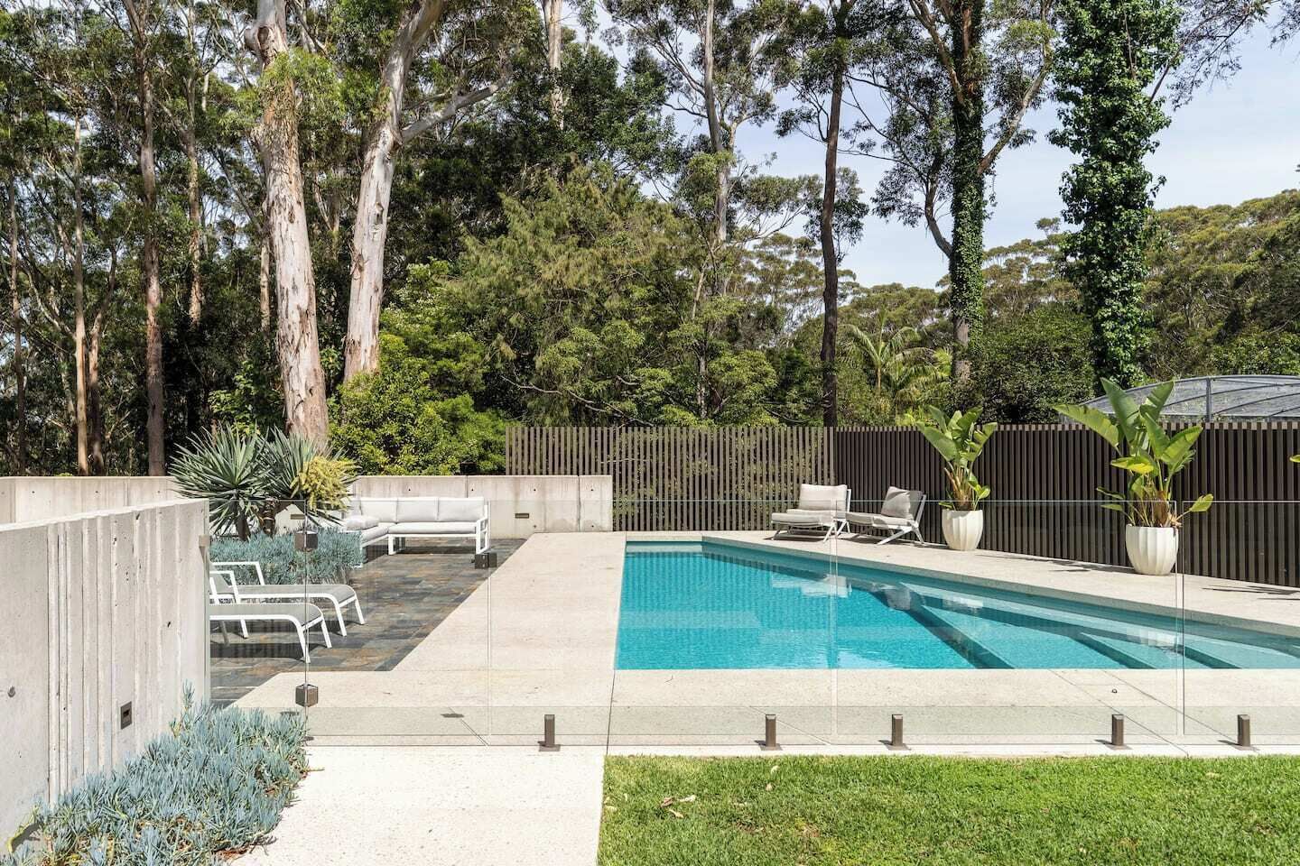 A backyard with a swimming pool, lounge chairs, and a wooden fence.