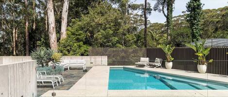 A backyard with a swimming pool, lounge chairs, and a wooden fence.