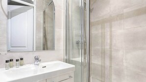 Un baño con cabina de ducha de vidrio, un lavamanos blanco con un espejo arriba y un mueble debajo.