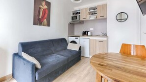 Una sala moderna con un sofá azul oscuro, una mesa de comedor de madera y una zona de cocina con armarios de madera clara y un microondas.