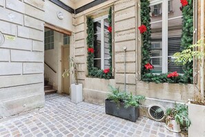 A stone building with a tiled courtyard, a staircase, and potted plants. - Appartement Cosy au coeur du Marais (Paris)
