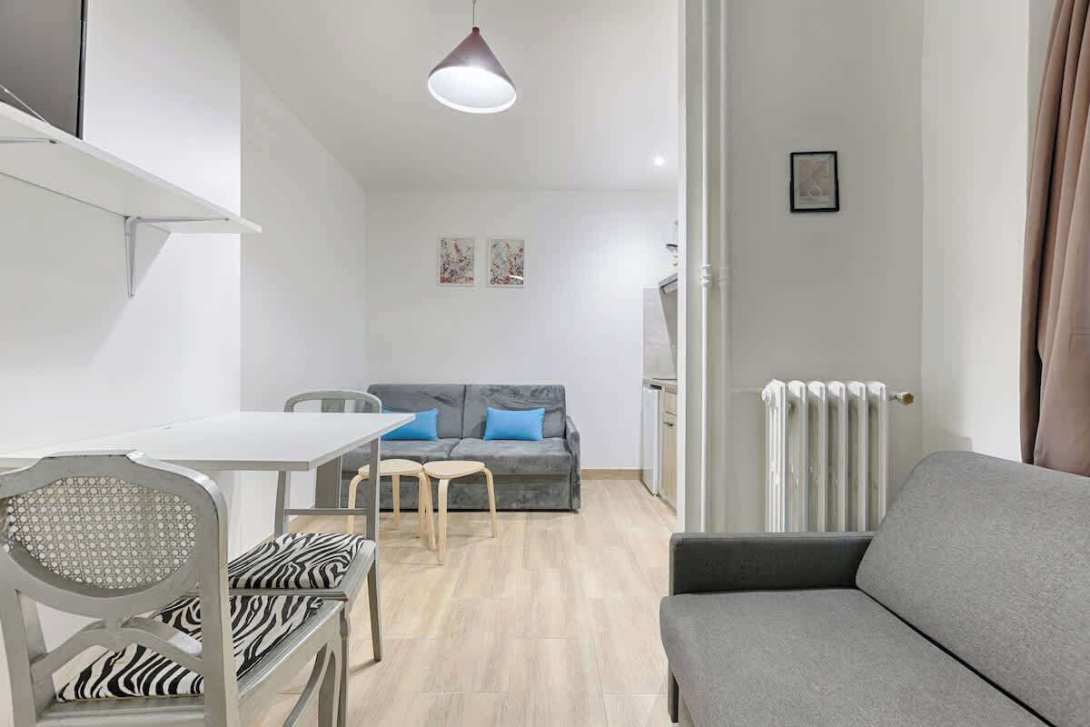 A modern living room with a grey sofa, a dining table with chairs, and a grey couch.