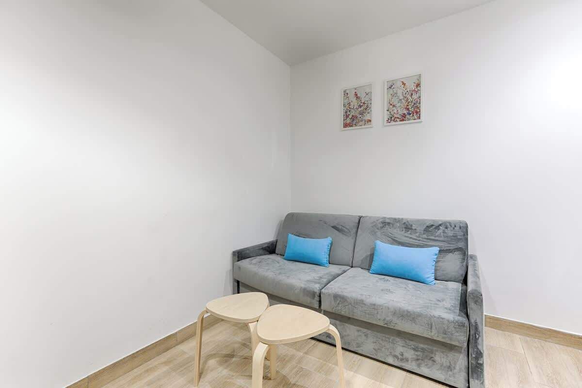 Una sala de estar moderna con un sofá gris, dos cojines azules y dos pequeñas mesas de madera.