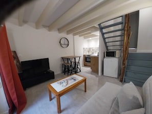 Un espacio habitable compacto con sofá, una mesa de centro, televisor, zona de cocina con microondas y una escalera.
