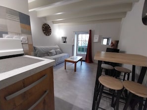 Una cocina moderna con horno integrado, un comedor con mesa de madera y taburetes de bar, y una sala de estar con sofá y un reloj en la pared.