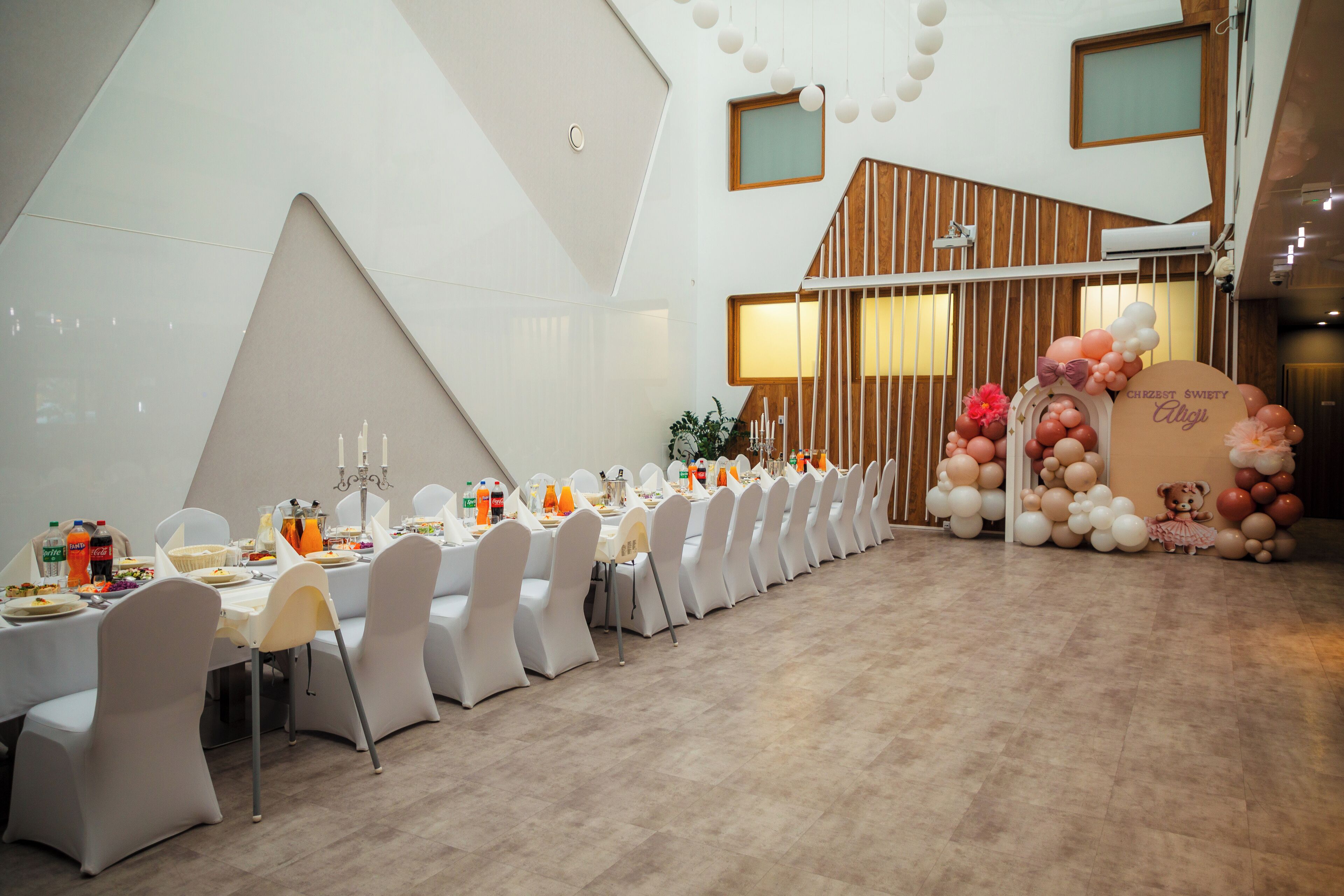 Una larga mesa de comedor con sillas blancas, un separador de madera y una decoración con globos.