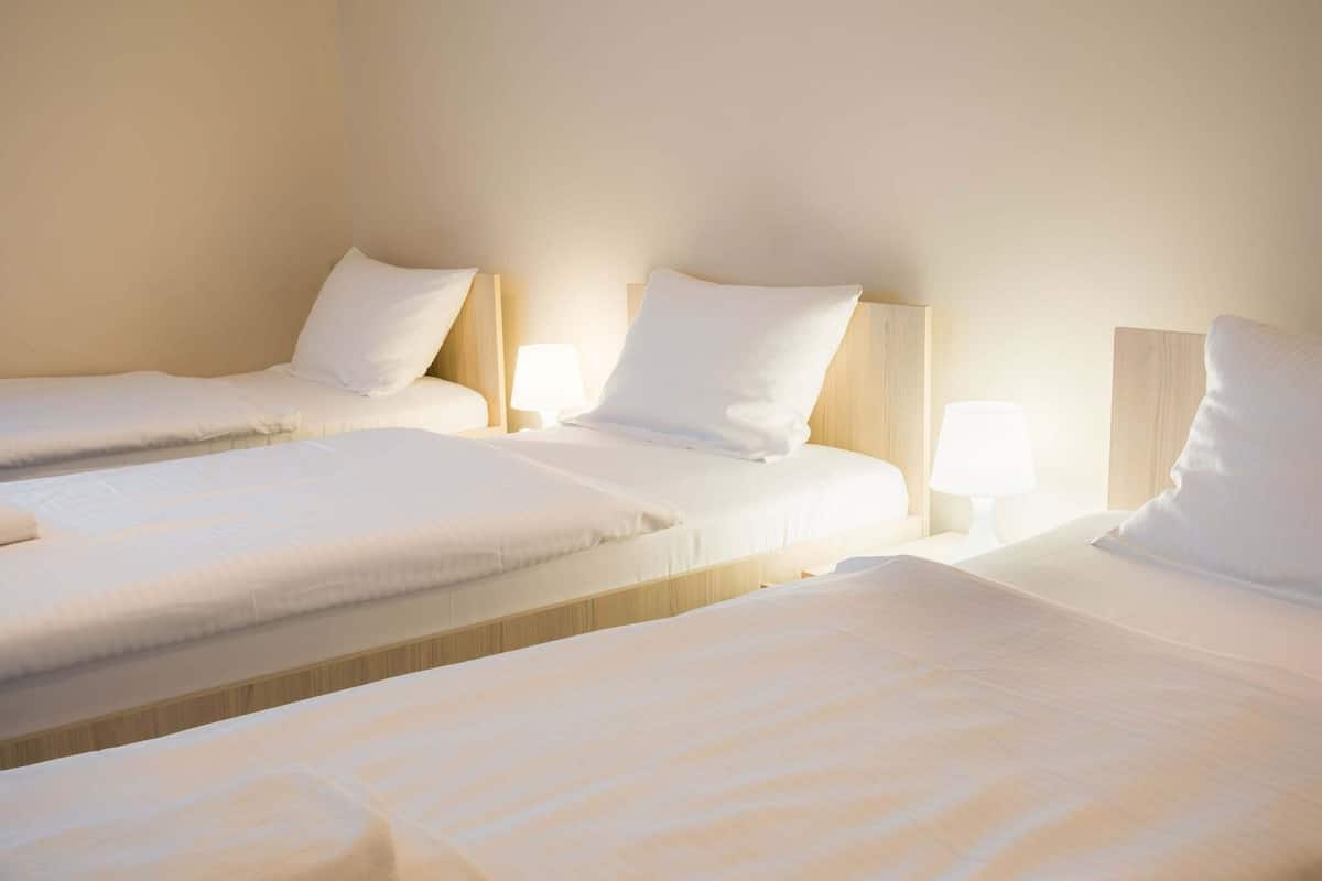 A hotel room with three single beds arranged in a row, each with a wooden headboard and white bedding.