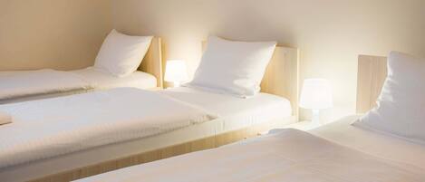 A hotel room with three single beds arranged in a row, each with a wooden headboard and white bedding.