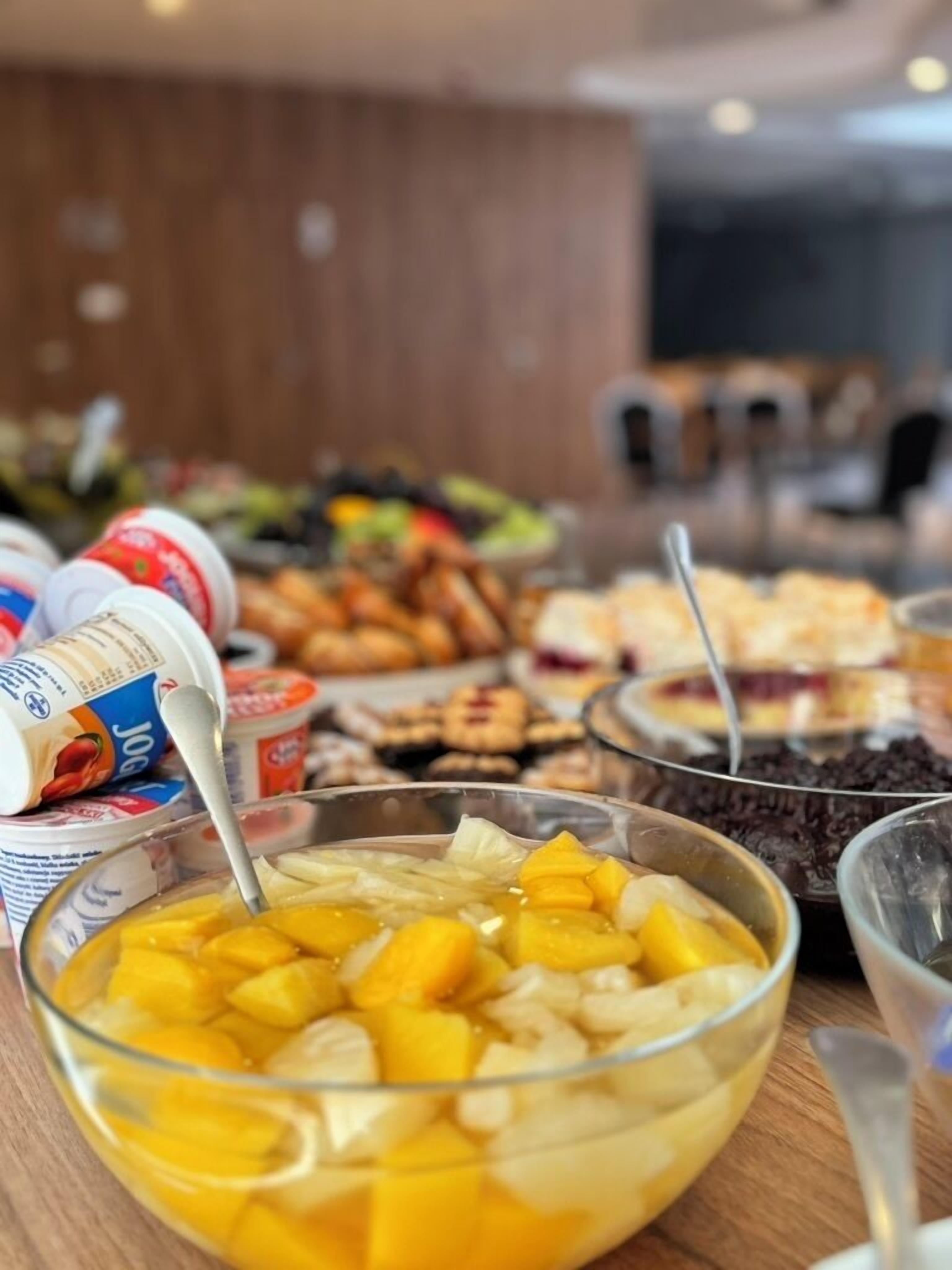 Un bufé con diversas opciones de comida, incluyendo un tazón de ensalada de frutas, yogur y otros platos.