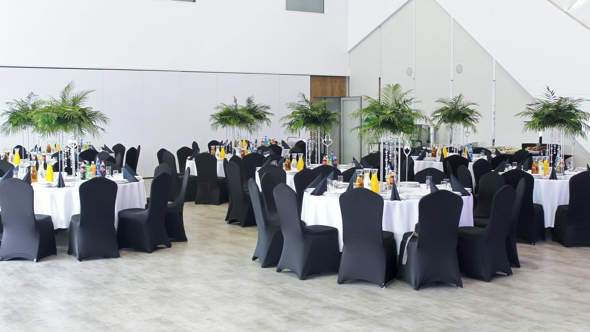 A banquet hall with round tables, black chairs, and white tablecloths.