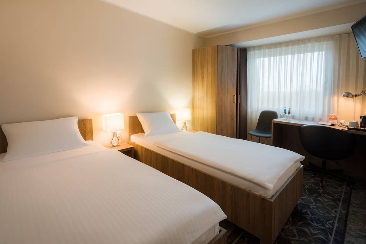 A hotel room with two beds, a desk, a chair, and a large window with curtains.