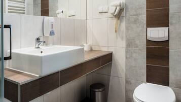 A modern bathroom with a white sink, a mirror, a toilet, and a trash bin.