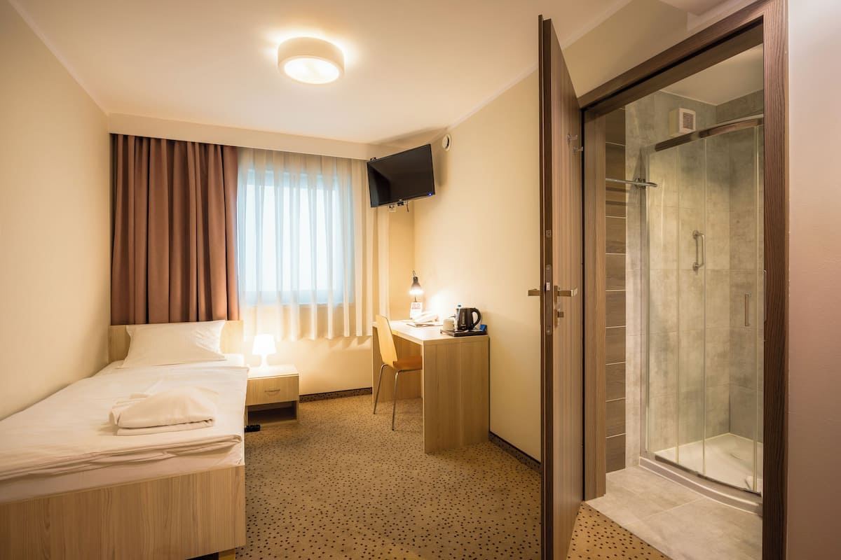 A hotel room with a bed, desk, chair, and a shower area.