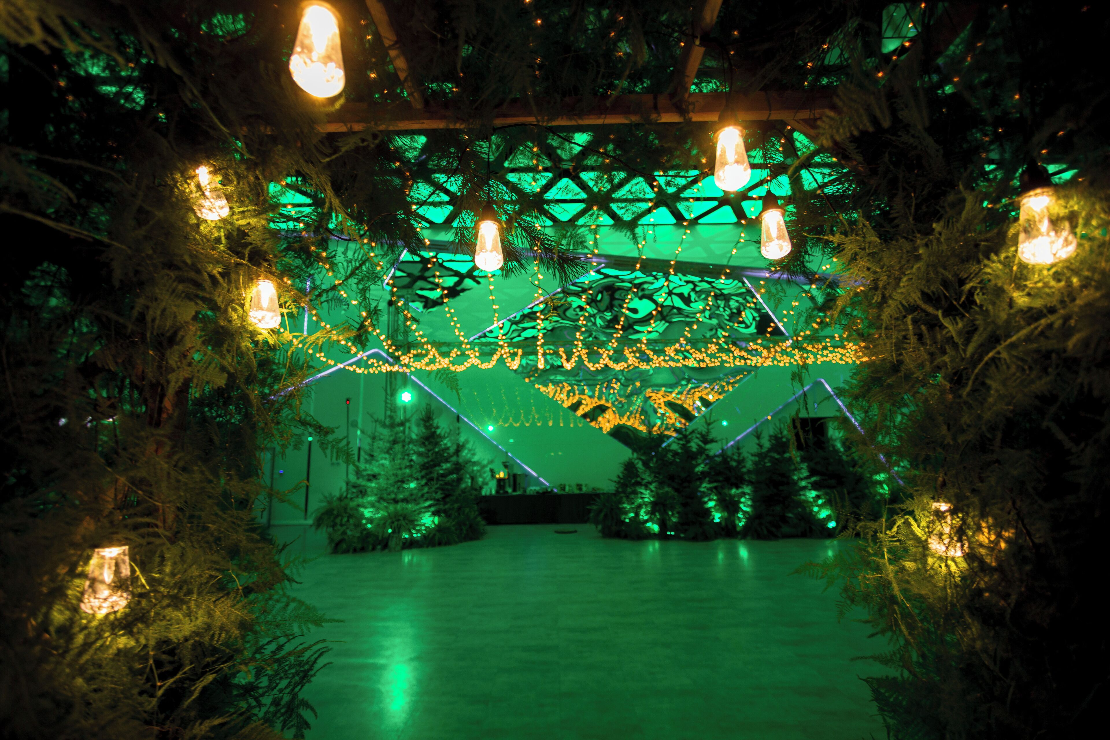 Una habitación con techo iluminado en verde, vigas de madera y lámparas colgantes.