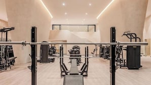 A modern gym with various exercise equipment, a central bench press, and a staircase leading to an upper level. - Presidential Suit 2 bedrooms All-Inclusive top ranked beautiful Hard Rock Hotel (Cancun)