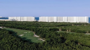 A golf course with a dense forest and a row of modern white buildings in the background. - Presidential Suit 2 bedrooms All-Inclusive top ranked beautiful Hard Rock Hotel (Cancun)