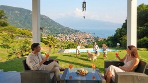 A terrace with wicker furniture, a pool, and a view of a coastal town. - D1MORA Sophie - LAKE VIEW villa with pool and large garden (Salò)