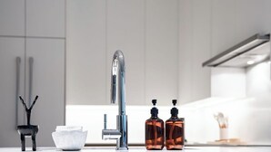 Una cocina moderna con un grifo de acero inoxidable, un cuenco blanco y dos botellas marrones sobre la encimera.