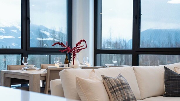 Un interior moderno con un sofá y una mesa de comedor, ventanas amplias con vistas a la montaña.