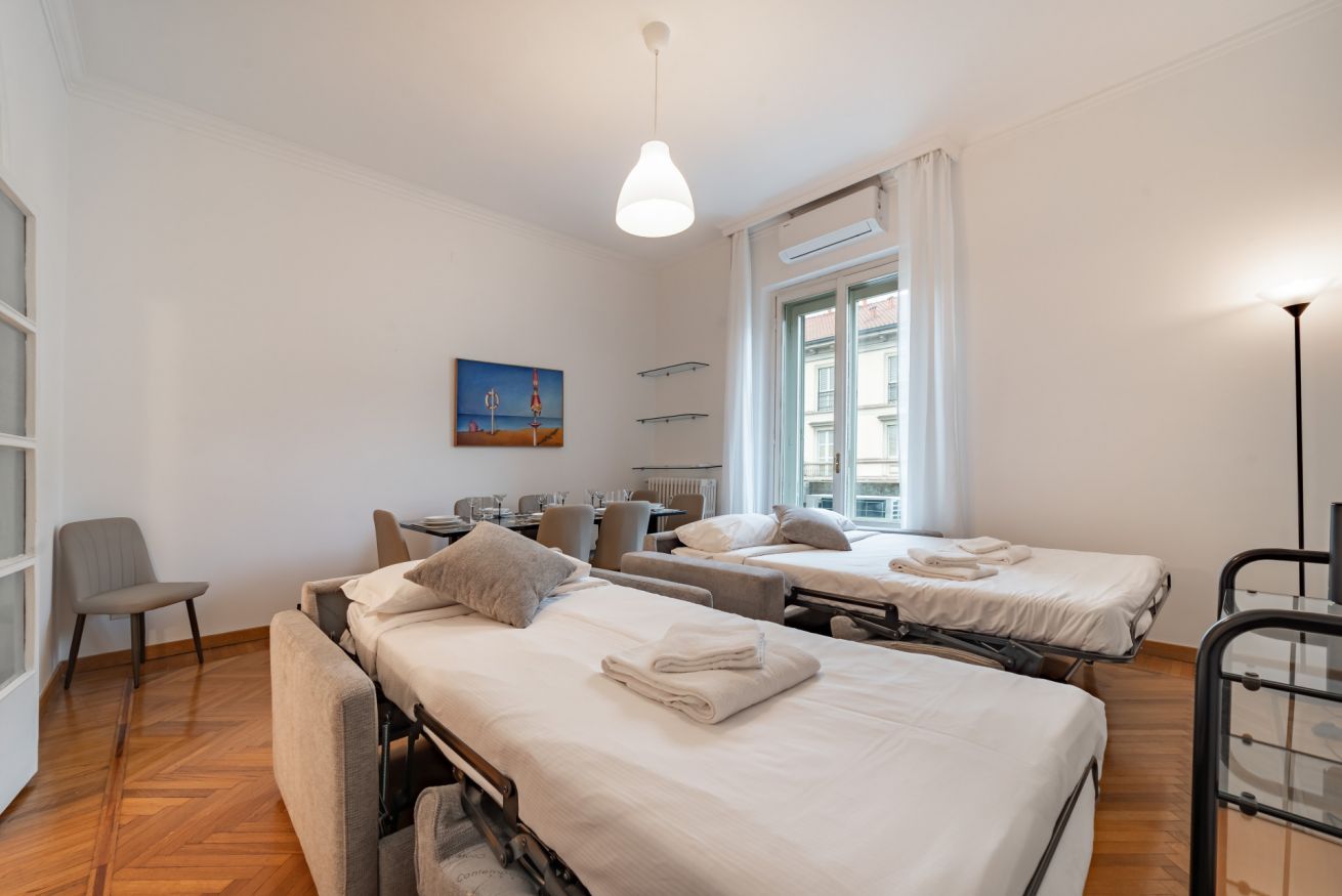 Ein Hotelzimmer mit zwei Betten, einem Sofa, einem Esstisch und einem Stuhl.