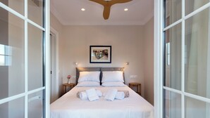 A neatly made bed with white linens and towels, a framed picture on the wall, and a ceiling fan. - Nancy Suites (Kassiopi)