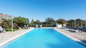 A rectangular swimming pool with a stone deck, surrounded by lounge chairs and a fence. - Nancy Suites (Kassiopi)