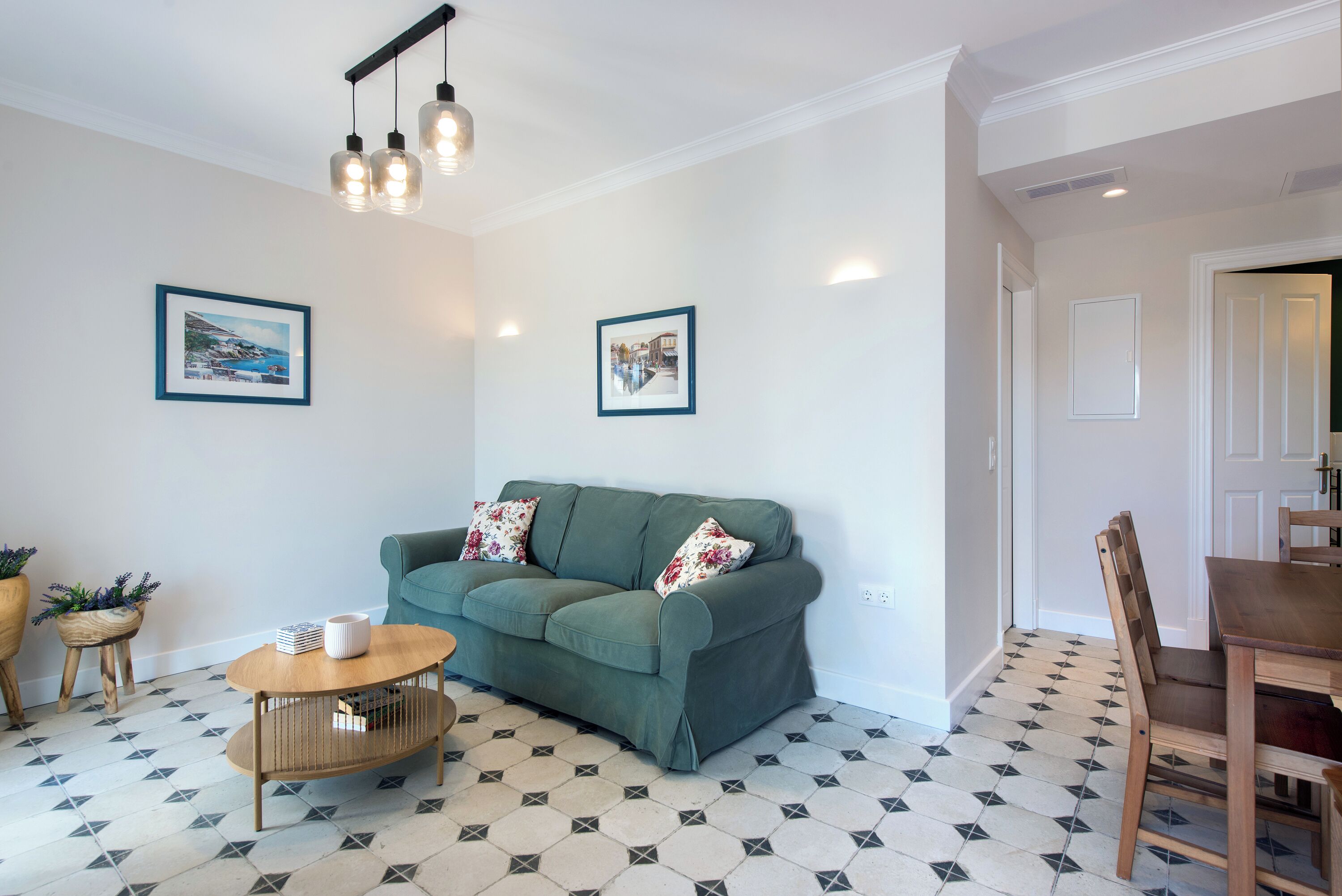 A living room with a green sofa, wooden coffee table, and two framed pictures on the wall.