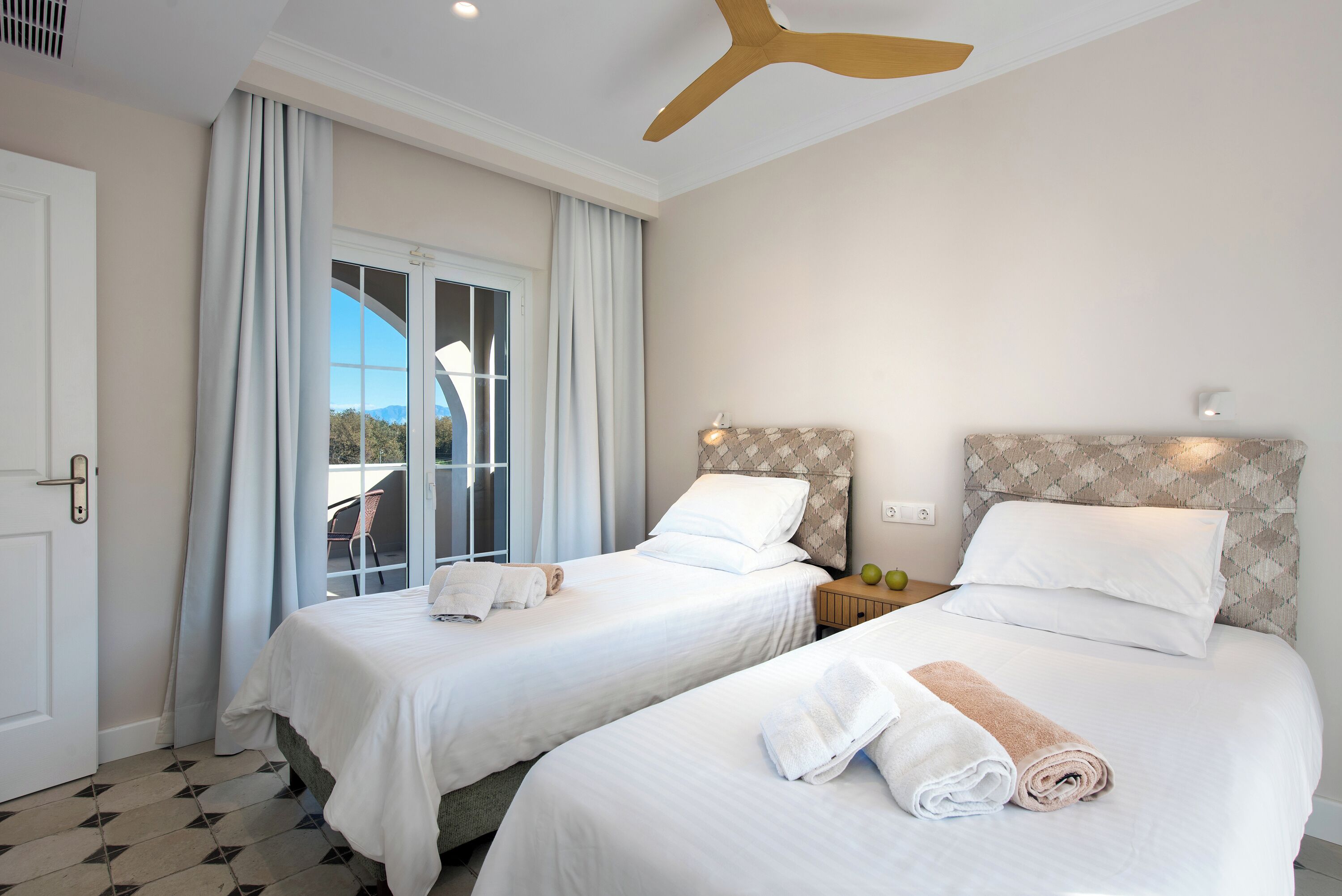 Une chambre d’hôtel avec deux lits, un ventilateur de plafond, une fenêtre avec des rideaux et une vue sur l’extérieur.