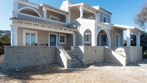 A multi-story house with a stone facade, multiple balconies, and a stone staircase leading to the entrance. - Nancy Suites (Kassiopi)