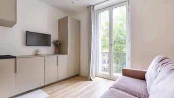 Un salon moderne avec un canapé, un téléviseur à écran plat fixé au mur et une porte-fenêtre coulissante donnant sur un balcon.