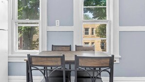 Un comedor con mesa y sillas, ventanas amplias y vistas a edificios.
