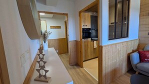 Un interior moderno con piso de madera, una recepción blanca, una zona de cocina y una sala de estar con un cojín rojo.