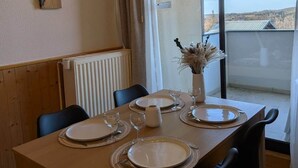 Un comedor con una mesa de madera dispuesta para seis personas, un jarrón con flores secas y vistas al campo a través de un ventanal grande.