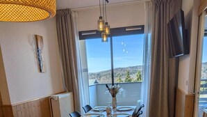 Un comedor con una mesa dispuesta para cuatro, un sofá con un cojín rojo y un televisor montado en la pared.