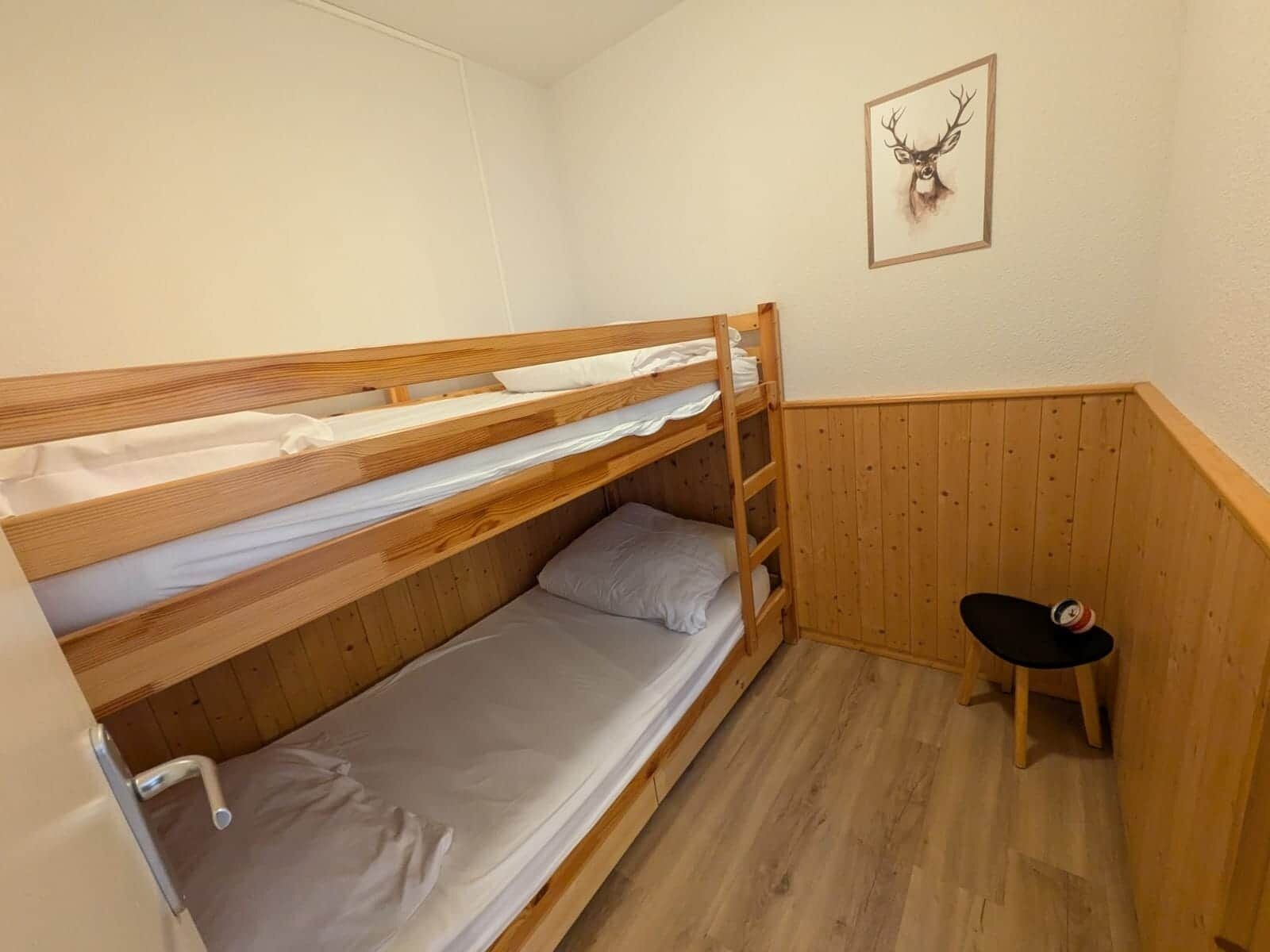 Une chambre avec des lits superposés, des murs en bois et un tableau représentant un cerf, encadré.