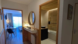 A modern hotel room with a wooden floor, a round mirror, a small sink, and a view of the outside. - Juracîmes Duo apartment for 2 people (Mijoux)