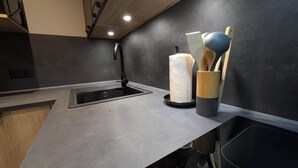 A modern kitchen with a black countertop, stainless steel sink, and wooden utensils in a holder. - Juracîmes Duo apartment for 2 people (Mijoux)