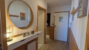 A hallway with wooden flooring, a round mirror, a small countertop with a towel, and a door leading to another room. - Juracîmes Duo apartment for 2 people (Mijoux)