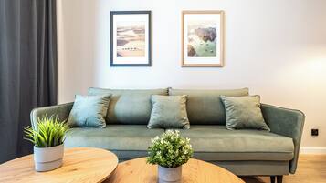 A modern living room with a green sofa, two framed pictures, and two potted plants on a wooden coffee table.
