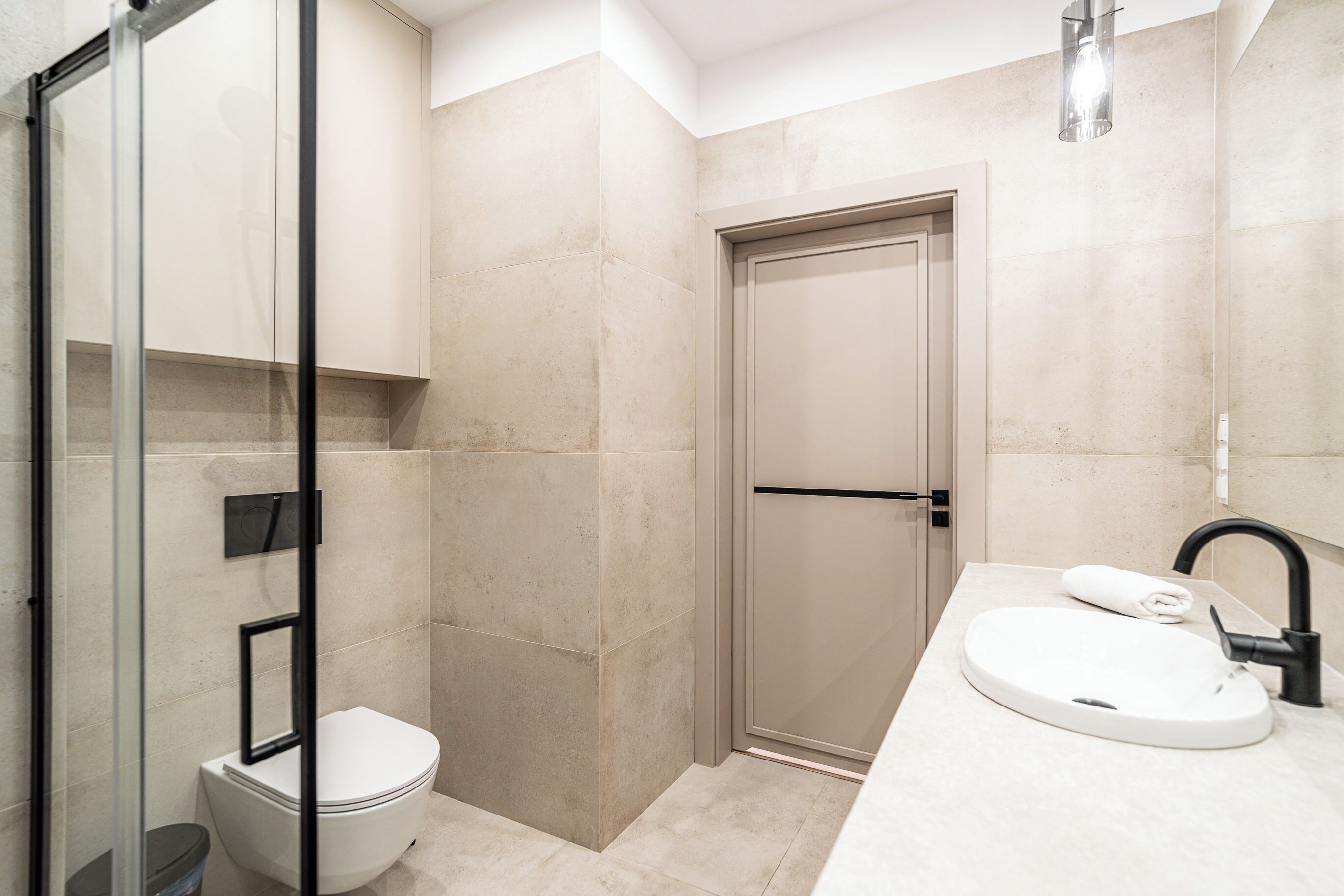 Une salle de bain moderne avec une douche à parois de verre, des toilettes blanches et un lavabo doté d’un robinet noir.