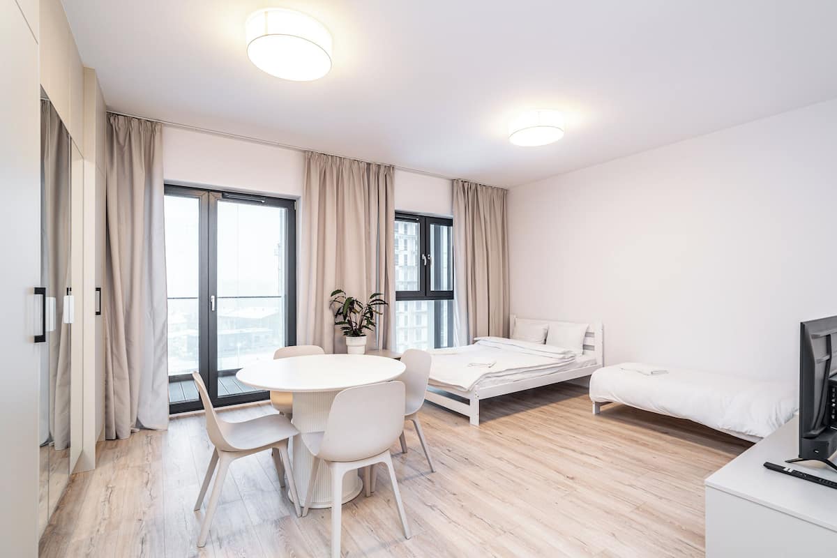 Ein modernes Hotelzimmer mit einem Bett, einem Schreibtisch, einem Stuhl, einem Esstisch und großen Fenstern.