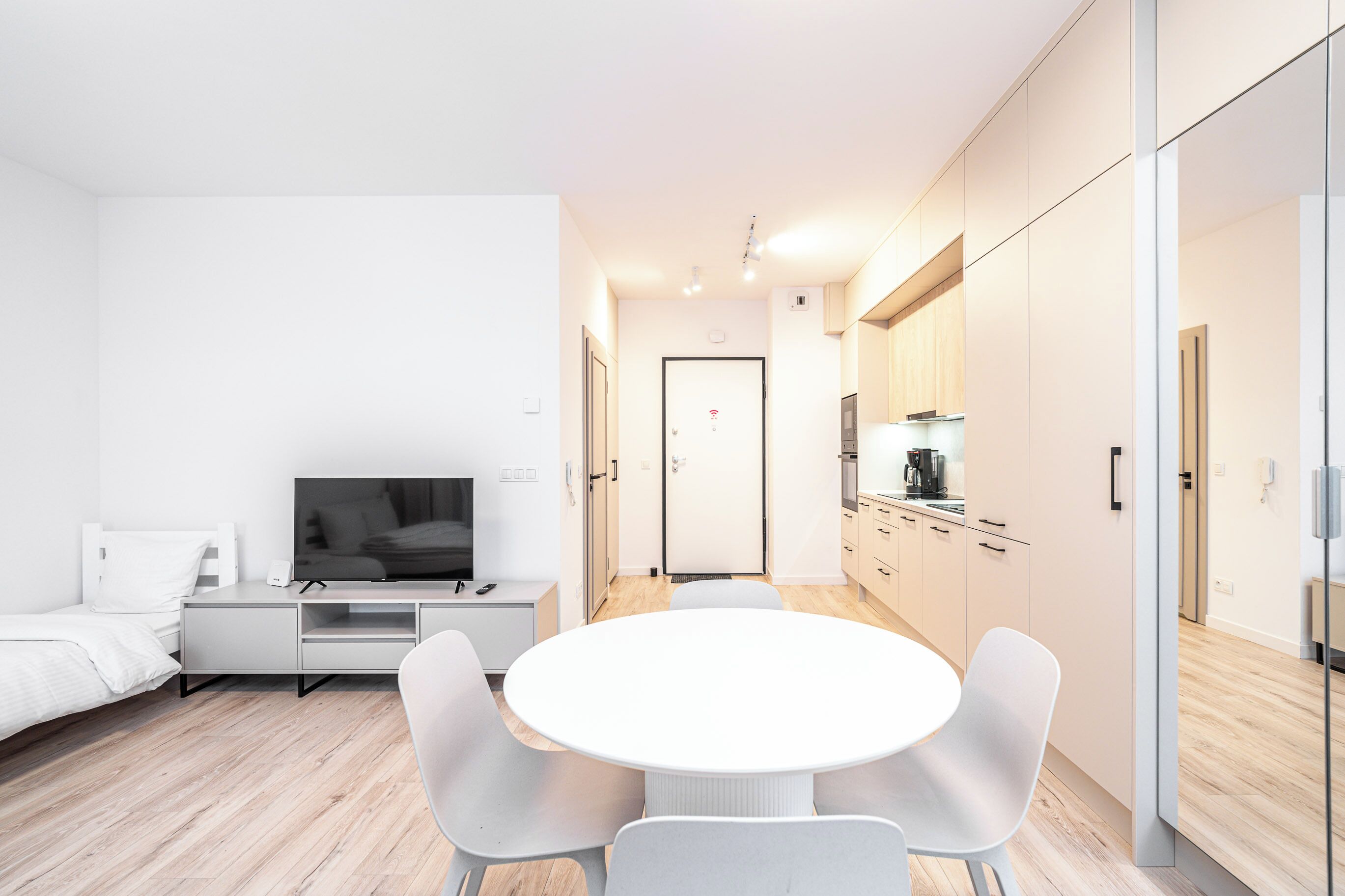 Ein stilvolles, minimalistisches Zimmer mit einem Bett, einem Fernseher, einem Esstisch und einer Küchenzeile.