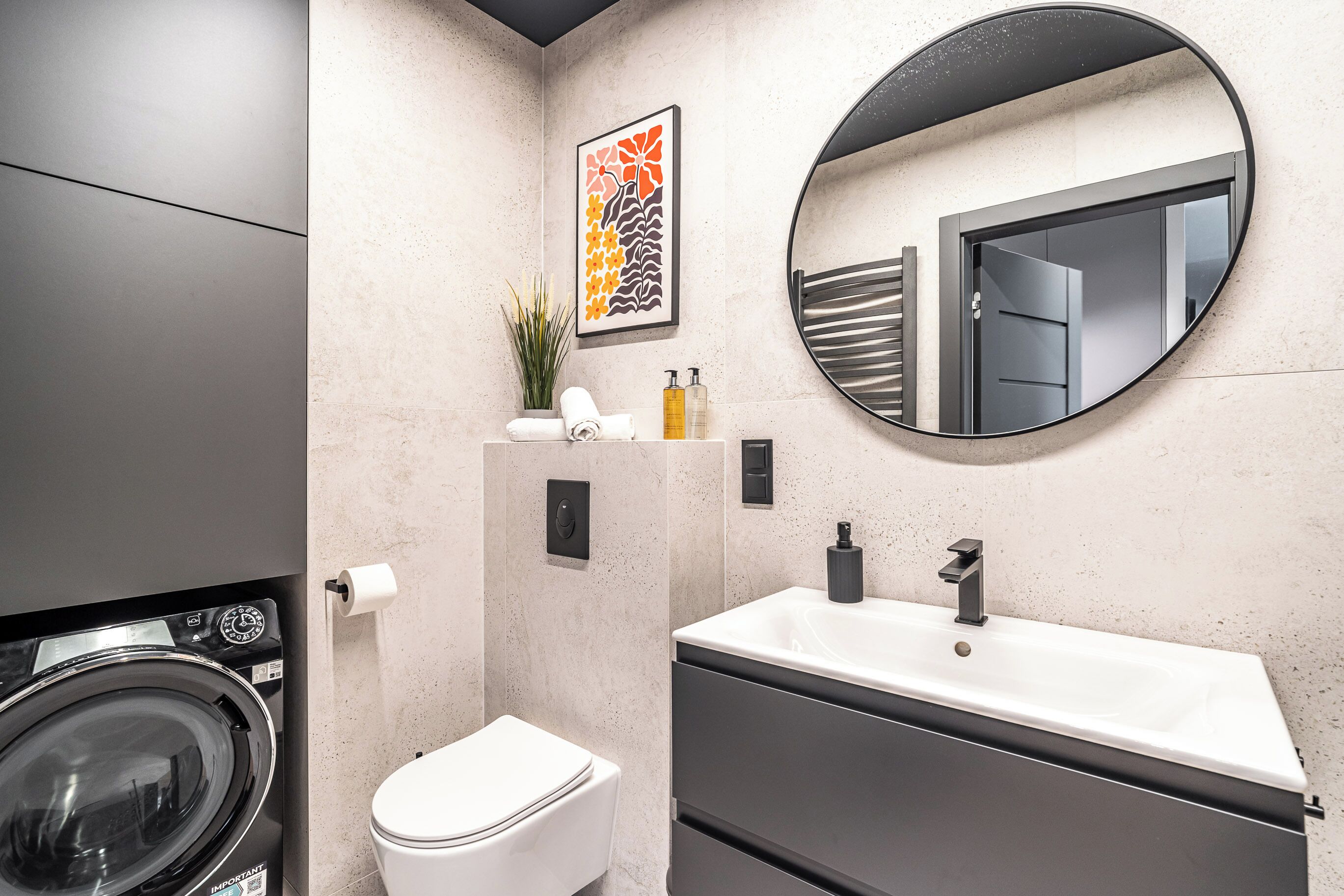 Un bagno moderno con lavatrice, toilette, lavandino e uno specchio grande.