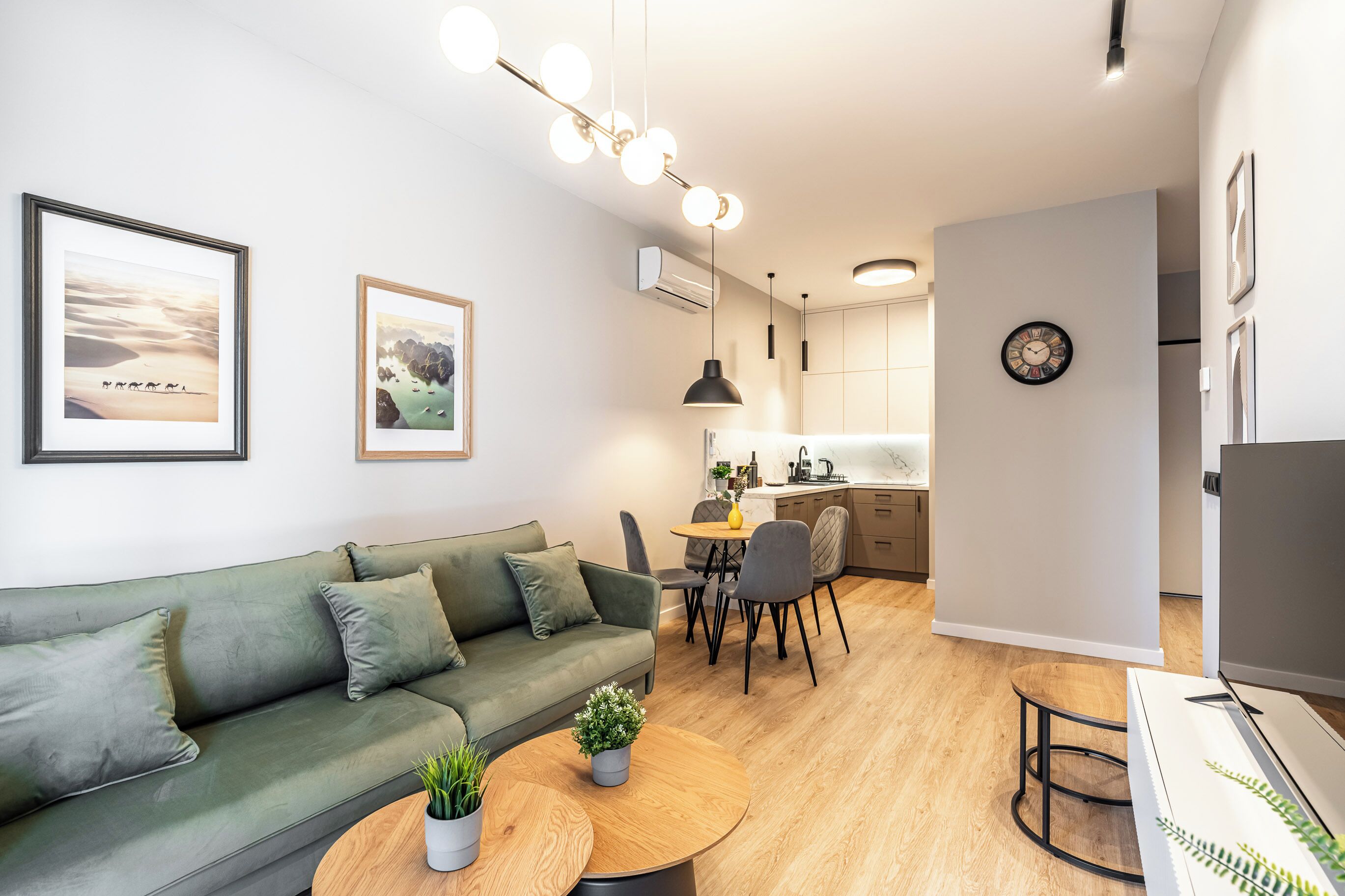A modern living room with a green sofa, a dining table, and a kitchen area in the background.