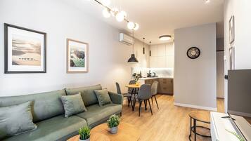 A modern living room with a green sofa, a dining table, and a kitchen area in the background.