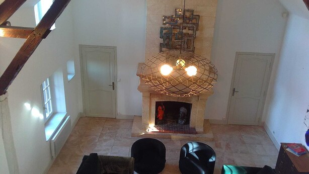 A high-ceilinged room with a stone fireplace, wooden beams, and a modern chandelier. - Villa La Ballière: Where memories are written between heaven and earth (Coullons)